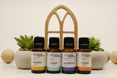 4 essential oils setting on table by plants, Protection, unwind, breathe free, and femease